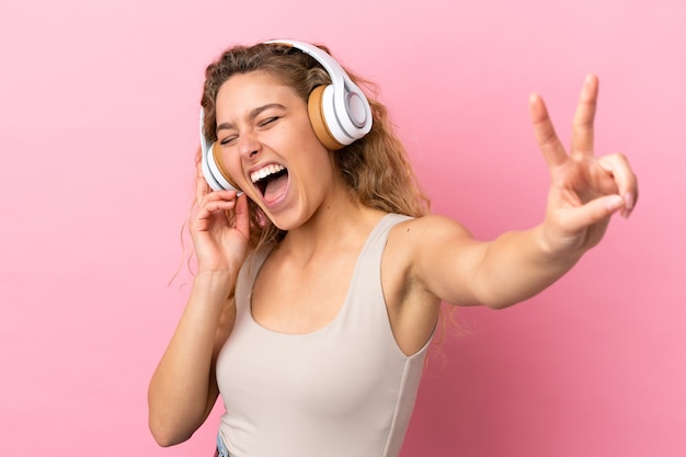 Junge blonde Frau isoliert auf rosa Hintergrund Musik hören und singen