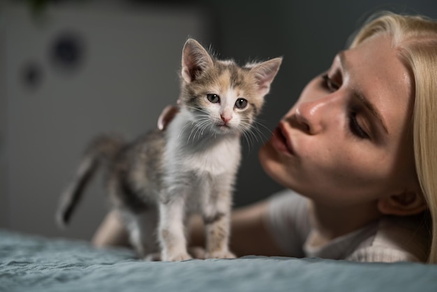 Junge blonde Frau küsst ihr kleines Kätzchen auf dem Bett. Liebe zu Haustieren zeigen, sich um Babykatzen kümmern.