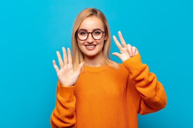 Junge blonde Frau lächelt und sieht freundlich aus, zeigt Nummer acht oder acht mit der Hand nach vorne, Countdown