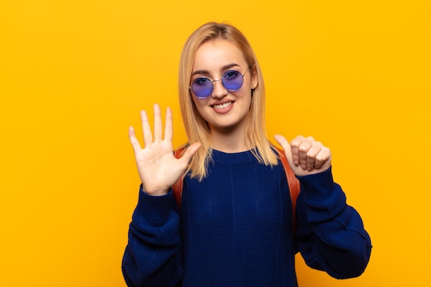 Junge blonde Frau lächelt und sieht freundlich aus, zeigt Nummer sechs oder sechste mit der Hand nach vorne, Countdown