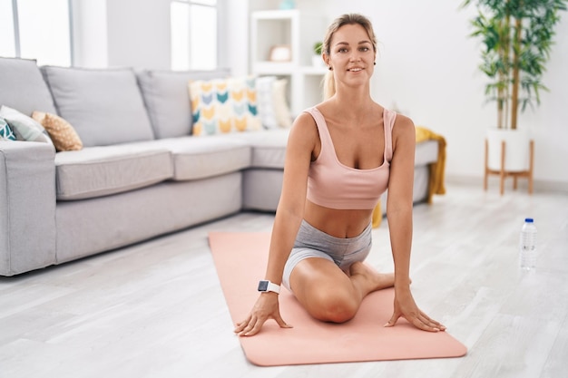 Junge blonde Frau lächelt zuversichtlich, Yoga-Übung zu Hause zu trainieren