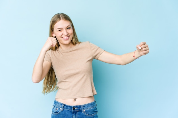 Junge blonde Frau lokalisiert auf blauem Wandtanzen und Spaß haben.