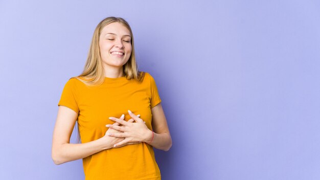 Junge blonde Frau lokalisiert auf lila Lachen, das Hände auf Herz hält, Konzept des Glücks.