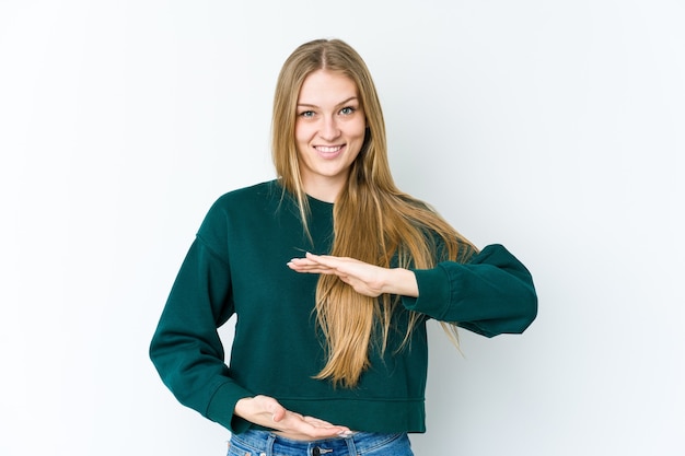 Junge blonde Frau lokalisiert auf weißer Wand, die etwas mit beiden Händen hält