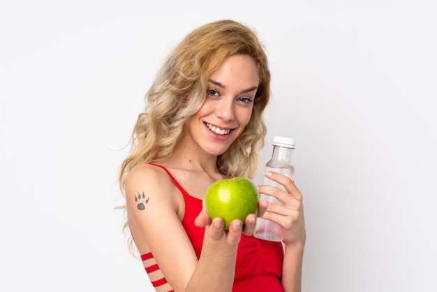 Junge blonde Frau lokalisiert auf weißer Wand mit einem Apfel und mit einer Flasche Wasser