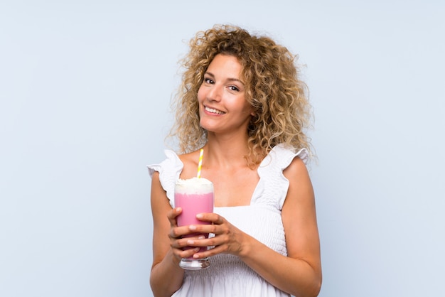 Junge blonde Frau mit dem lockigen Haar, das ein Erdbeeremilchshake anhält