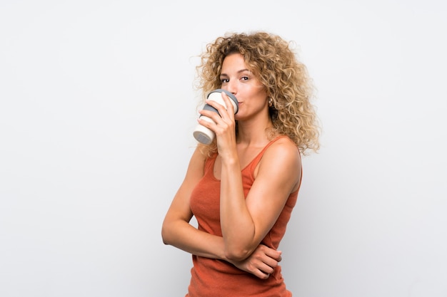 Junge blonde Frau mit dem lockigen Haar, das einen Mitnehmerkaffee anhält