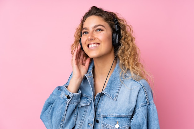 Junge blonde Frau mit dem lockigen Haar lokalisiert auf rosa Hörmusik