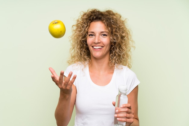 Junge blonde Frau mit dem lockigen Haar mit einem Apfel und mit einer Flasche Wasser