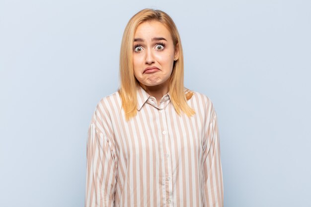 Junge blonde Frau mit einem albernen, verrückten, überraschten Gesichtsausdruck, aufgedunsenen Wangen, die sich vollgestopft, fett und voller Essen fühlt