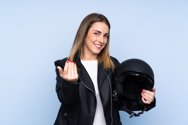 Junge blonde Frau mit einem Motorradsturzhelm über der getrennten Wand, die einlädt, mit der Hand zu kommen. Schön, dass Sie gekommen sind