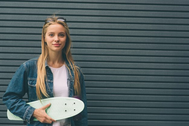 Junge blonde Frau mit einem Skateboard in seiner Hand gegen den Hintergrund