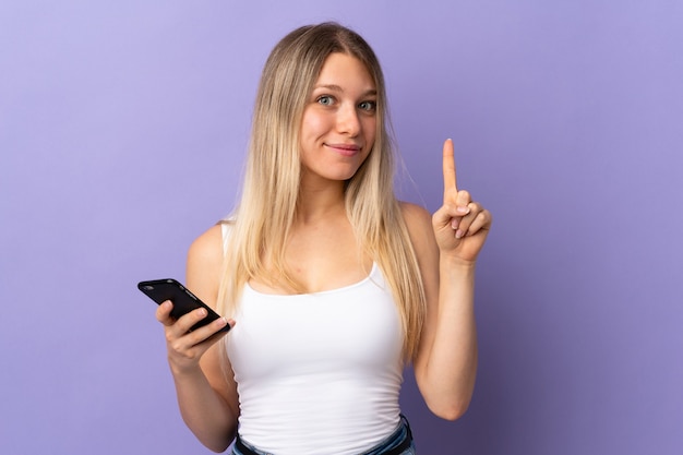 Junge blonde Frau mit Handy lokalisiert auf lila zeigt mit dem Zeigefinger eine tolle Idee