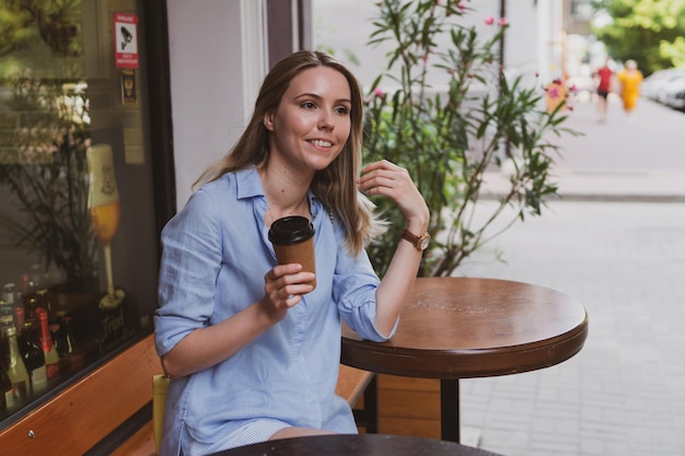 Junge blonde Frau mit Kaffee in einem Straßencafé im Sommer