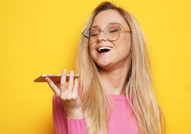 Junge blonde frau mit rosa pullover mit handy auf gelbem hintergrund