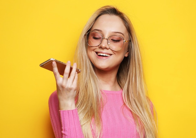 Junge blonde Frau mit rosa Pullover mit Handy auf gelbem Hintergrund