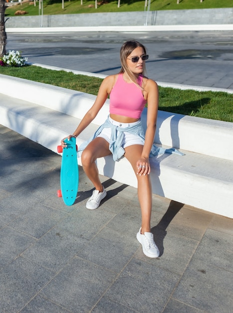 Junge blonde Frau mit Skateboard draußen am hellen sonnigen Sommertag