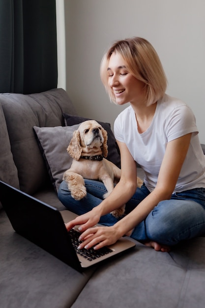 junge blonde Frau mit Spaniel sitzt an einem Laptop-Blogger und arbeitet im Internet-Home-Office