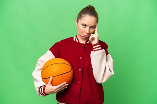 Junge blonde Frau spielt Basketball vor isoliertem Chroma-Key-Hintergrund und denkt an eine Idee