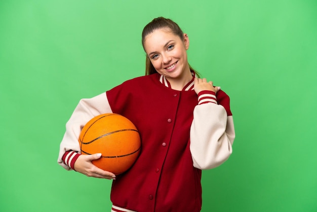 Junge blonde Frau spielt Basketball vor isoliertem Chroma-Key-Hintergrund und lacht