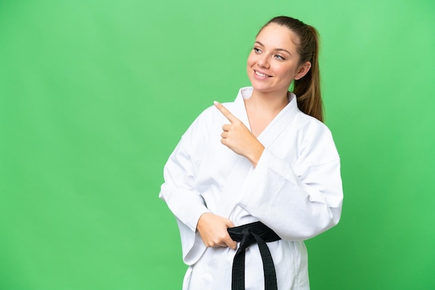 Junge blonde Frau über isoliertem Chroma-Key-Hintergrund, die Karate macht und auf die Seite zeigt