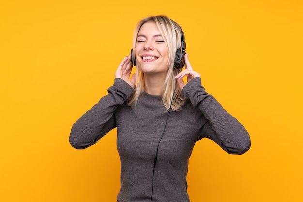 Junge blonde Frau über isolierter gelber Wand, die Musik hört und singt