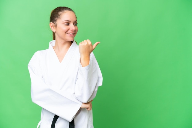 Junge blonde Frau vor isoliertem Chroma-Key-Hintergrund, die zur Seite zeigt, um ein Produkt zu präsentieren