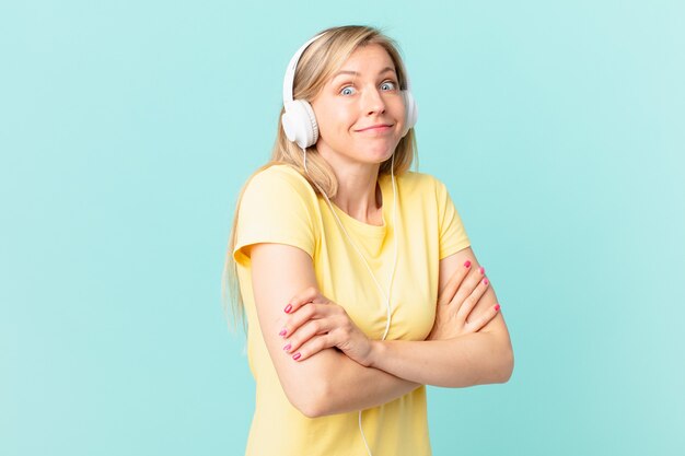 Junge blonde Frau zuckt mit den Schultern, fühlt sich verwirrt und unsicher und hört Musik.