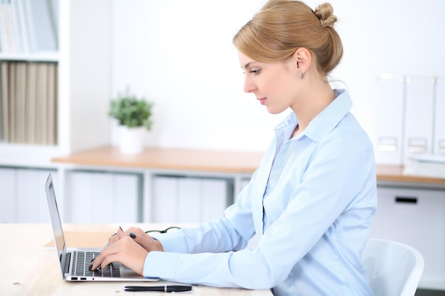 Junge blonde Geschäftsfrau mit Laptop im Büro. Unternehmenskonzept.