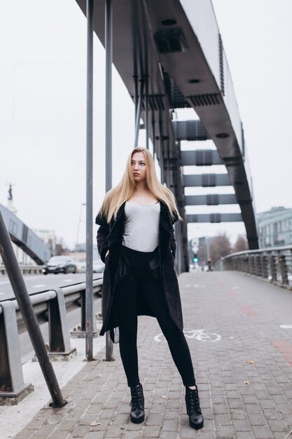 Junge blonde Geschäftsfrau nahe Brücke. Wandern entlang der europäischen Stadt