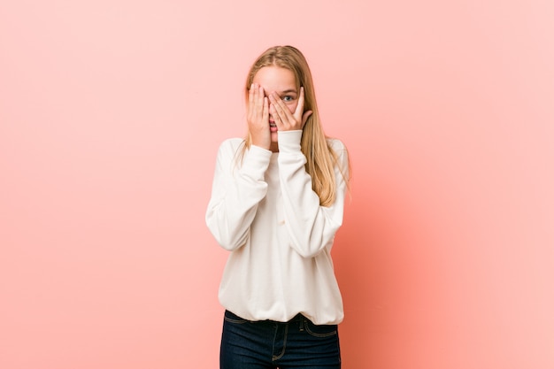 Junge blonde Jugendlichfrau blinken durch die Finger, die erschrocken und nervös sind.