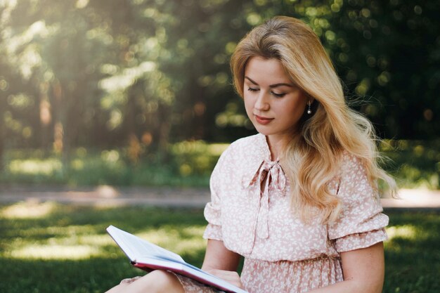 Junge blonde junge Frau im Park liest ein Buch