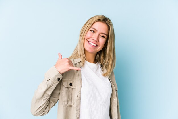 Junge blonde kaukasische Frau, die eine Handy-Anrufgeste mit den Fingern zeigt.