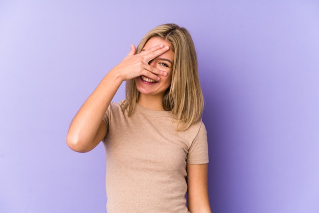 Junge blonde kaukasische Frau isoliert blinzeln durch durch Finger, verlegenes bedeckendes Gesicht.