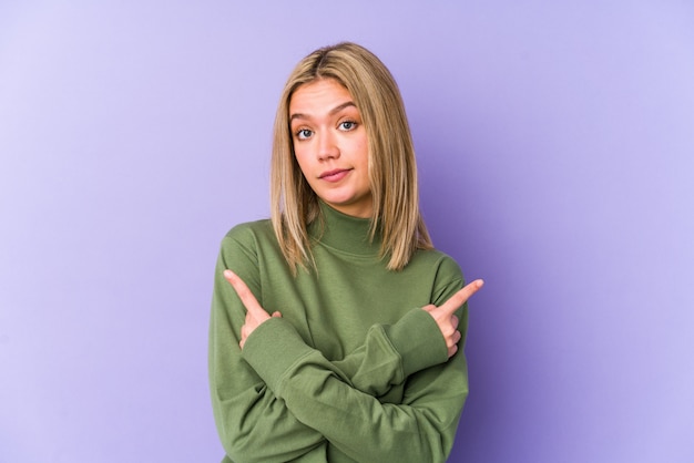 Junge blonde kaukasische Frau isolierte Punkte seitwärts, versucht, zwischen zwei Optionen zu wählen.