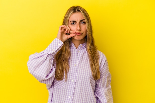 Junge blonde kaukasische Frau mit den Fingern auf den Lippen, die ein Geheimnis halten.