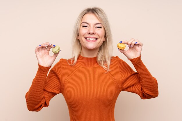 Junge blonde russische Frau, die bunte französische Macarons hält