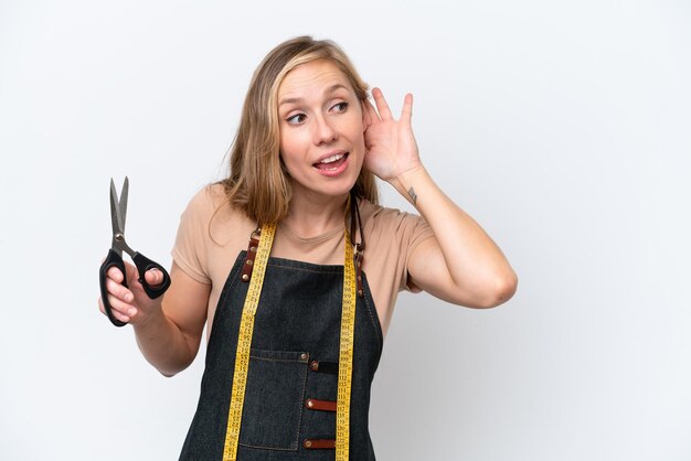 Foto junge blonde schneiderin isoliert auf weißem hintergrund, die etwas hört, indem sie die hand auf das ohr legt