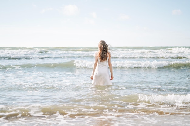 Junge blonde schöne Frau mit langen Haaren im weißen Kleid genießt das Leben am Meeresstrand