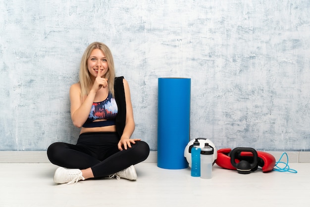 Junge blonde Sportfrau, die auf dem Boden tut Ruhegeste sitzt