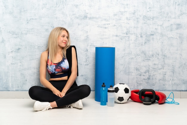 Junge blonde Sportfrau, die auf dem Bodenlachen sitzt