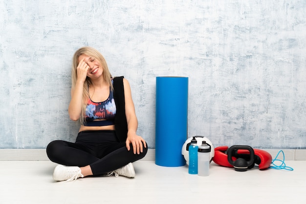 Junge blonde Sportfrau, die auf dem Bodenlachen sitzt