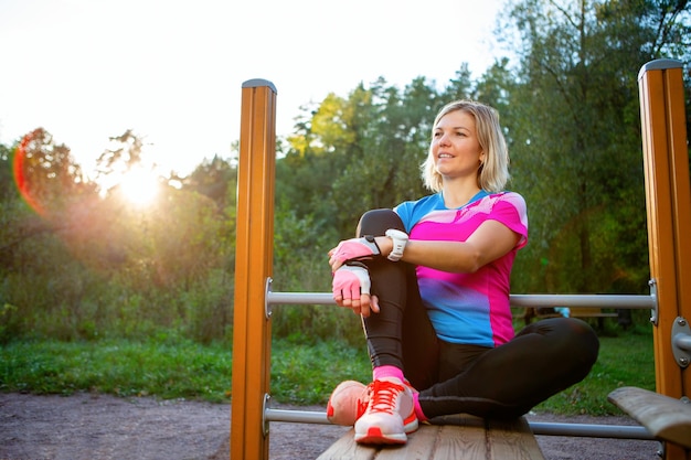 Junge blonde Sportlerin, die am Sommermorgen auf einer Holzbank im Park sitzt und wegschaut