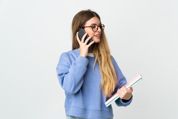 Junge blonde Studentin auf Weiß, die ein Gespräch mit dem Handy hält