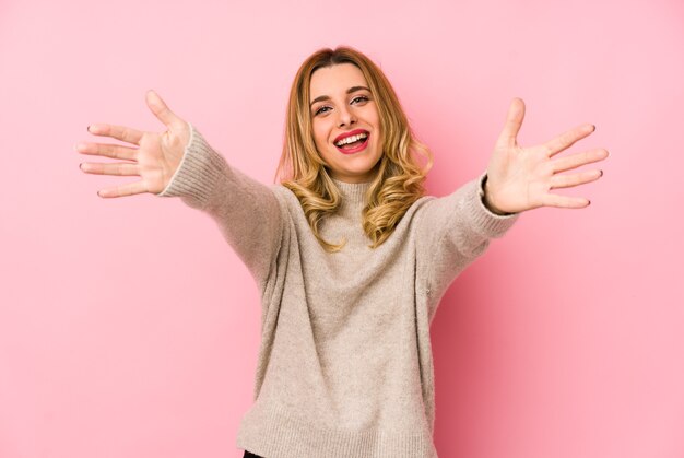 Junge blonde süße Frau, die einen Pullover isoliert trägt, fühlt sich zuversichtlich, die Kamera zu umarmen.