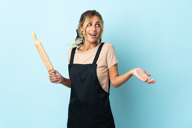 Junge blonde uruguayische Kochfrau lokalisiert auf blauer Wand mit Überraschungsausdruck beim Betrachten der Seite