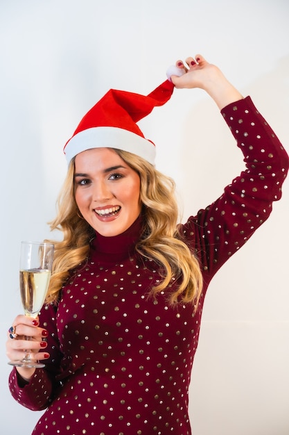 Junge blondhaarige Dame in einer Weihnachtsmütze, die einen festlichen Toast mit einem Glas Champagner macht