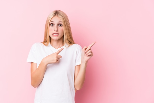 Junge Blondine auf der rosa Wand entsetzten das Zeigen mit den Zeigefingern auf einen Kopienraum.