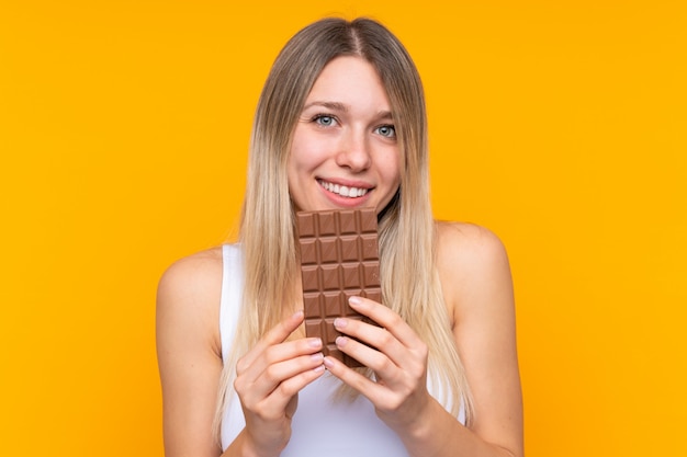 Junge Blondine, die eine Schokoladentablette und -glücklich nehmen