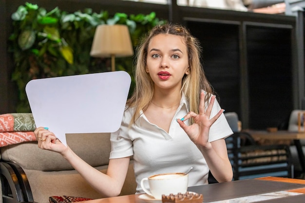 Junge Blondine, die weißes Ideenbrett hält und OK gestikuliert